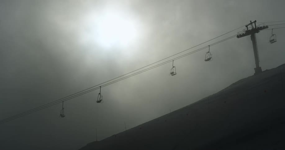 A ski lift on a hill with dark clouds above