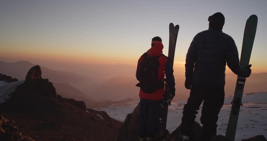 Skiers standing on top of mountain peak admiring the sunrise
