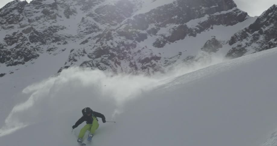 A skier sends up a cloud of snow as they ski down a mountain slope on a sunny day