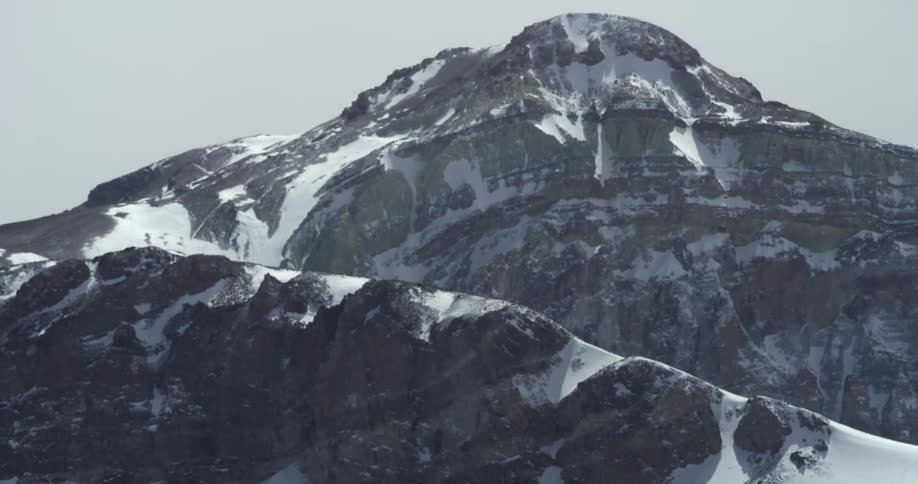 The wind blows alongside a rocky snowby mountain