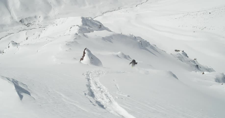 A man flies by the camera and skis down a steep slope