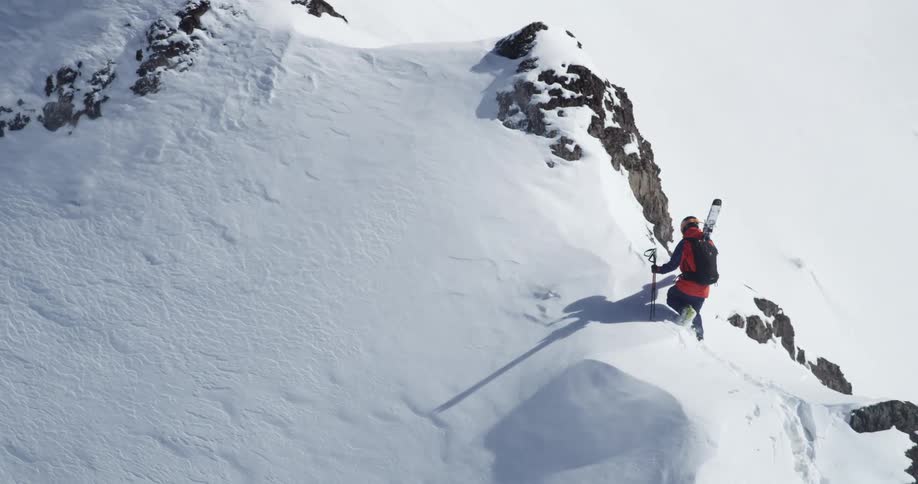 A lone skier hikes up a snowy mountainside on a winter day