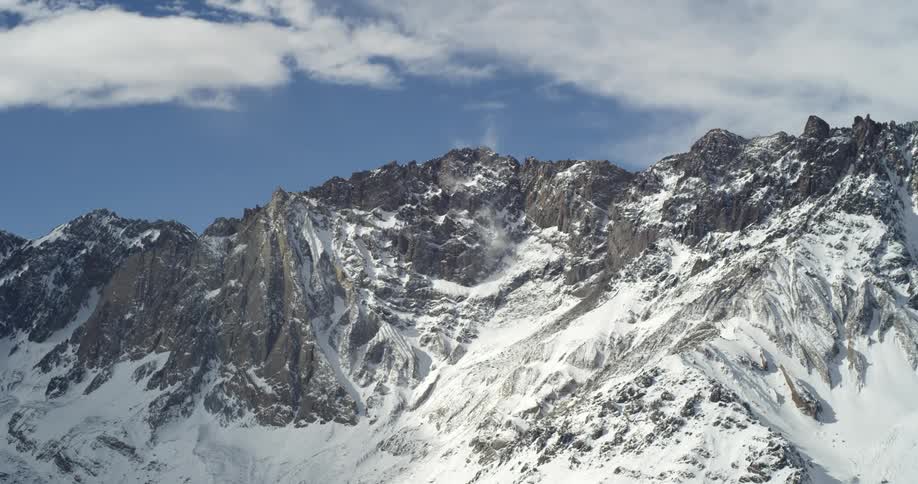 Snow covers slopes of huge mountain under cloudy sky