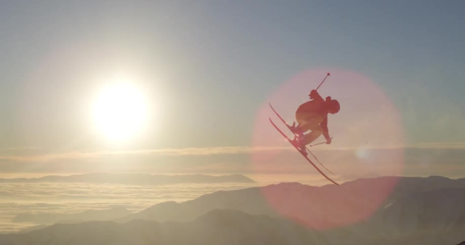 A skier goes over a jump in snowy mountains on a sunny day