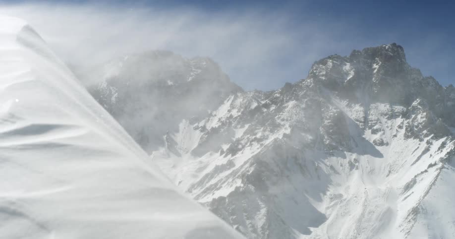 Blowing snow near snow covered mountains under a blue sky