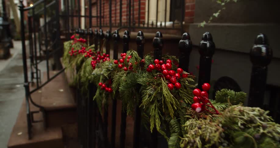 Artificial berry and greenery decorate iron work fence near brownstone steps
