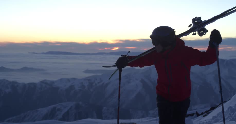 A male skier hikes up a mountain at sunset
