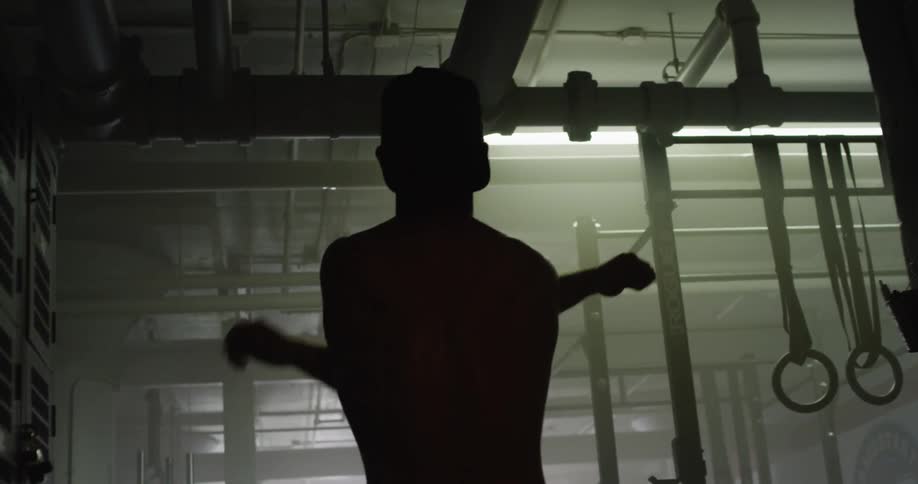 A man in a backward baseball cap swings his arms back and forth as he stretches in a gym