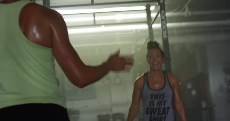 A pair of sweating women in athletic wear high five one another as they pass each other in a gym