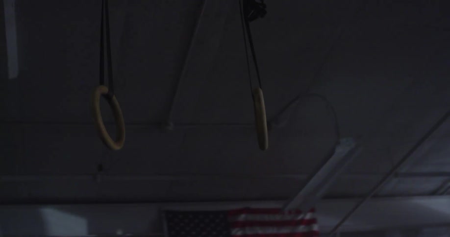 A pair of steady rings hang from the ceiling of a dimly lit gym as a light flashes repeatedly in the background
