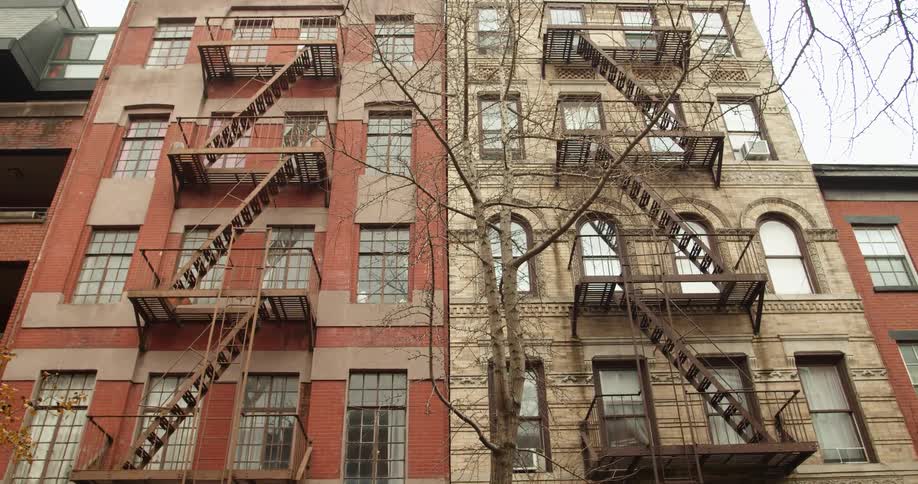 Fire escapes occupy sides of side by side apartment buildings under pale sky