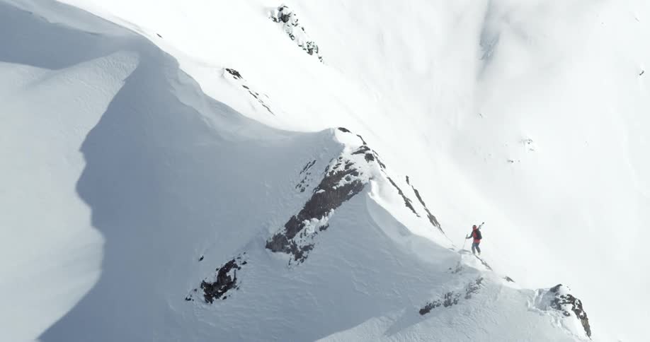 A snow covered mountain range with a skier walking on the slope