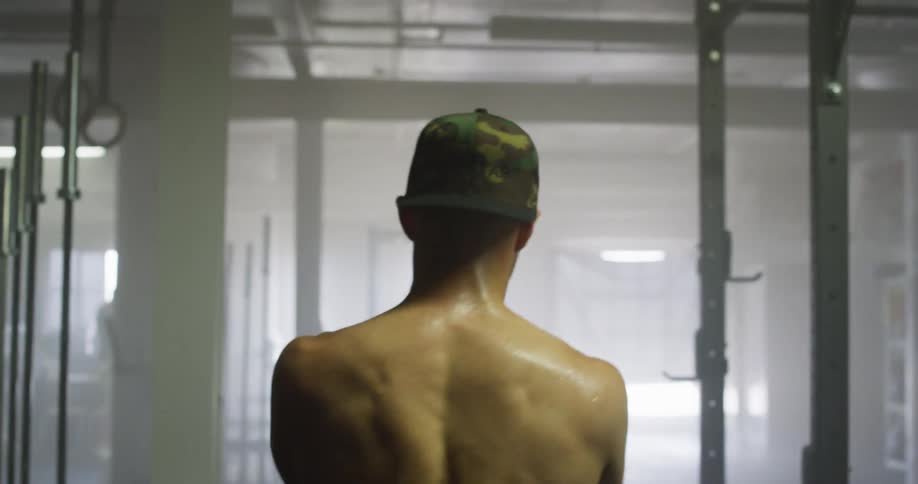 Sweaty muscular man with a cap walks in gym