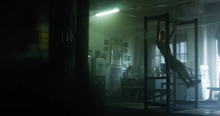 Shirtless muscular man does pull ups in a gym
