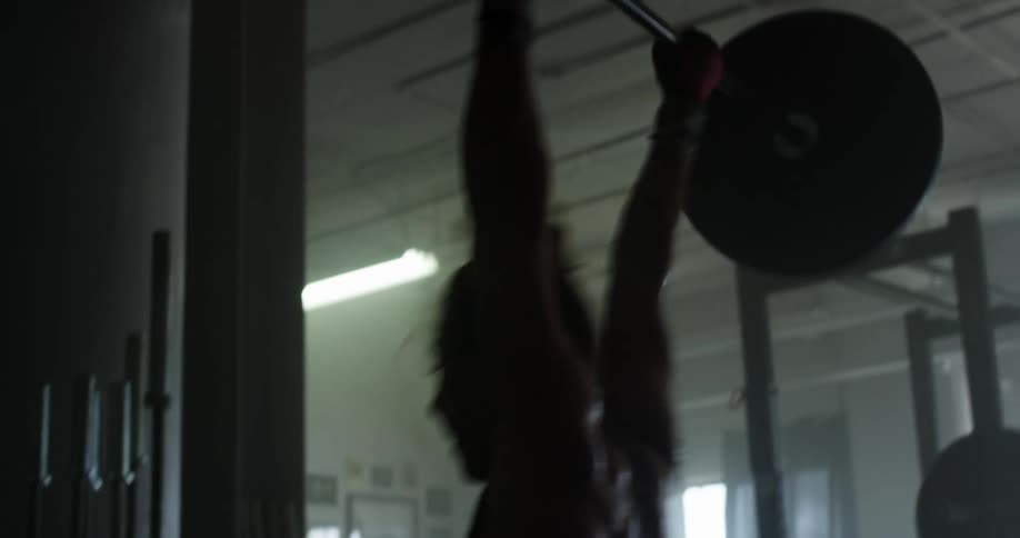 A woman lifts a barbell with large weights on the ends as flashing lights illuminate her in a dimly lit gym