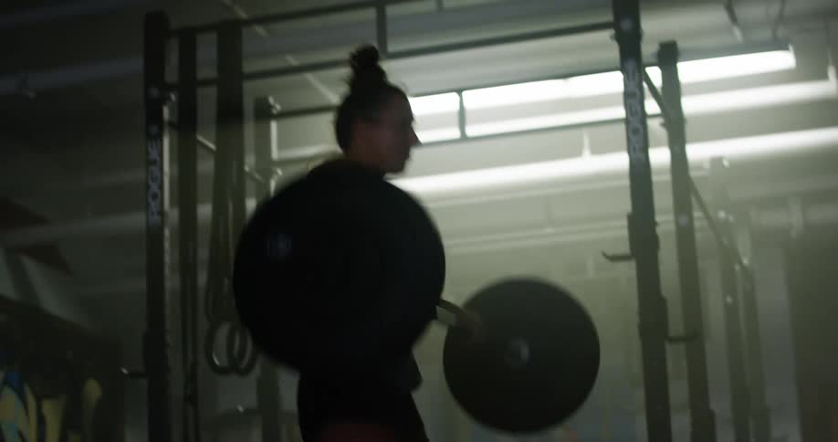 Woman lifts heavy weight bar in dimly lit gym