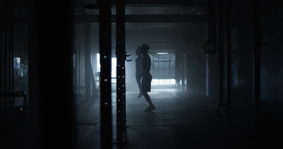 Man and woman jumping ropes in gym are silhouetted against the window light