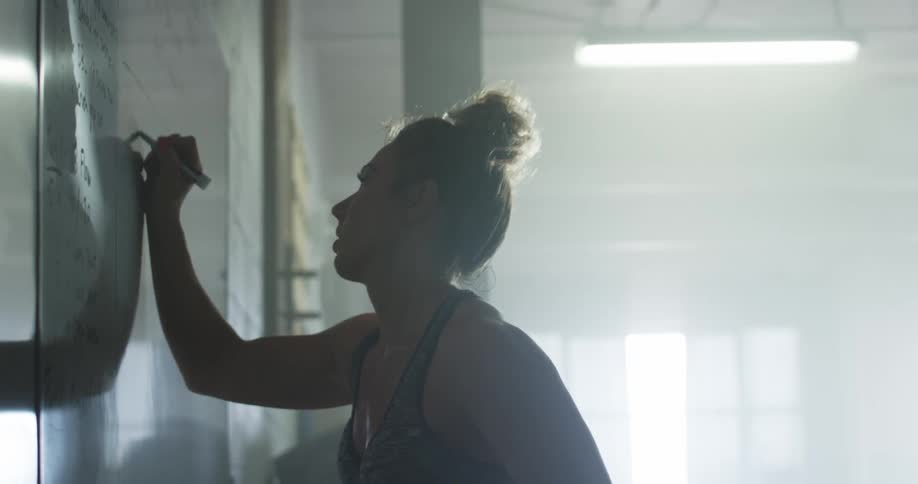 Side view of a woman with a top knot hair and a sports top writing on a white board