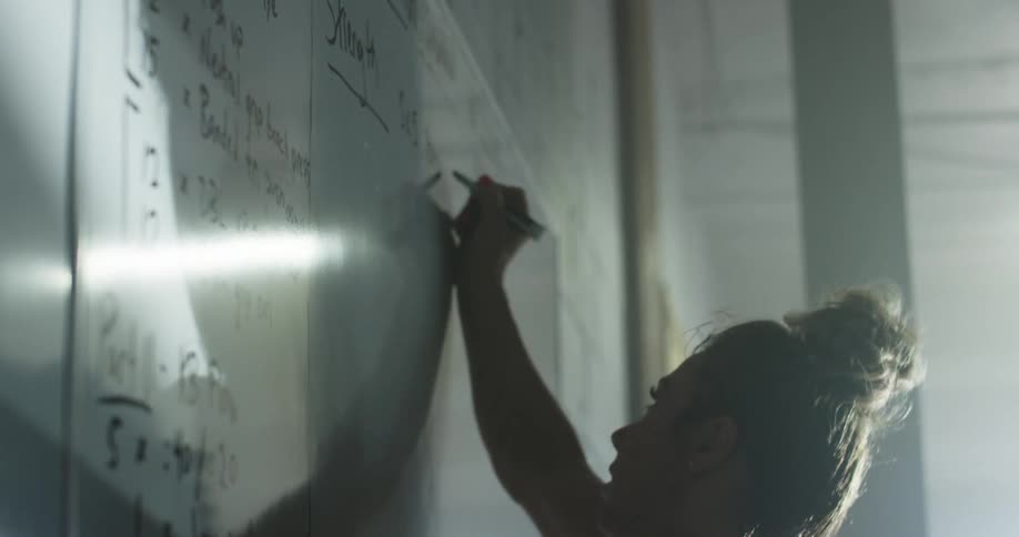 Woman writing on a whiteboard using a black marker in a dimly lit room