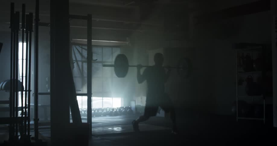A man in a gym lifting weights with a window in the background