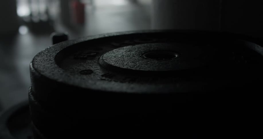 Inside of a darkly lit weight room the lights are blinking and illuminate large weight plates