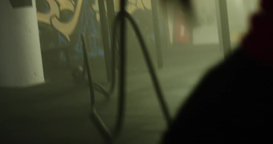 A man in a gym working out with ropes with a wall with graffiti in the background