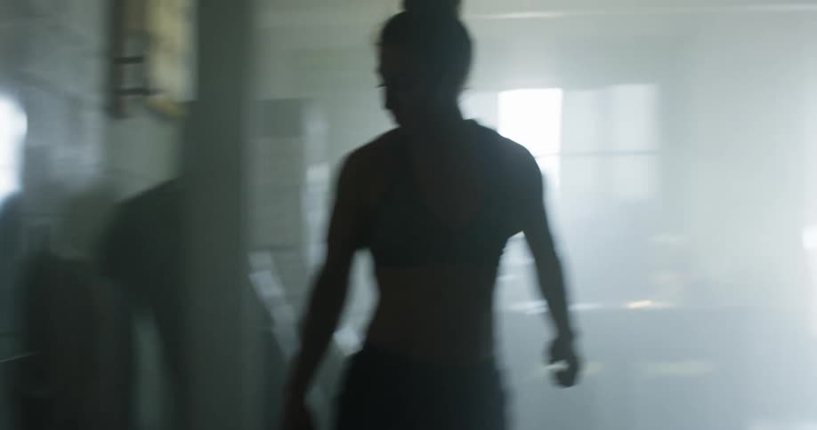 A woman in athletic wear writes on a white board before turning away and walking across a dimly lit gym