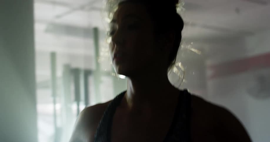 Muscular woman warming up before working out is silhouetted against sunlight in gym