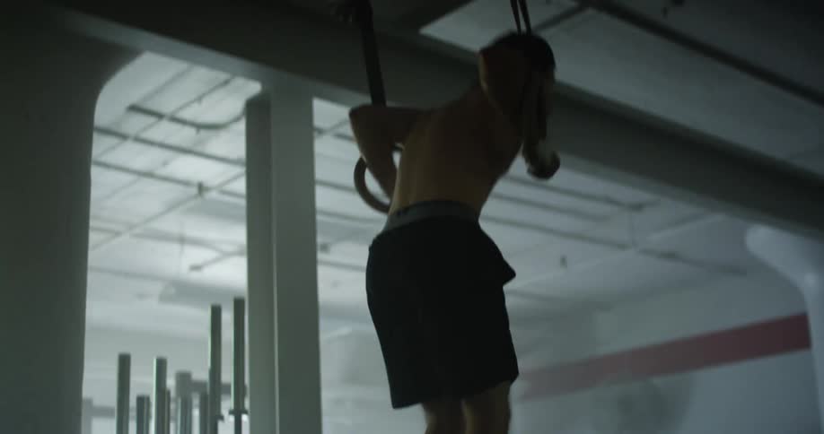 Man exercises using hanging rings in dimly lit gym