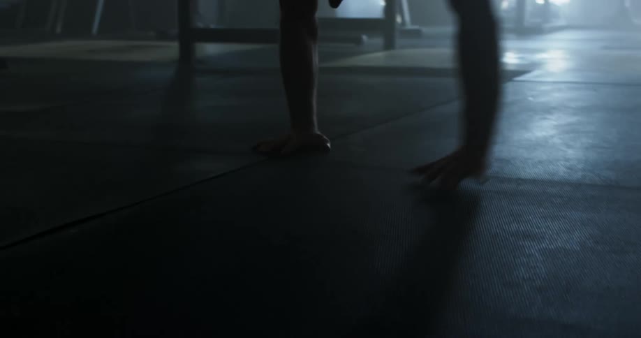 Man wearing baseball cap walks on hands in dimly lit gym
