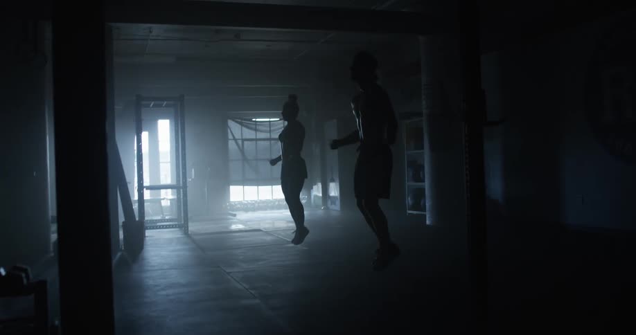 A man and woman are jump roping indoors