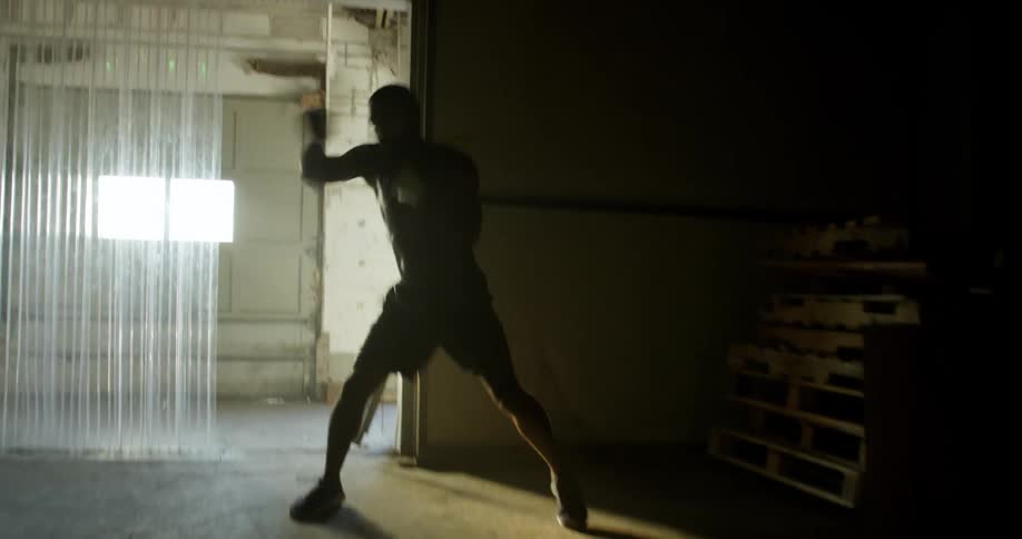 A man boxes in the air quickly in a dark basement like room