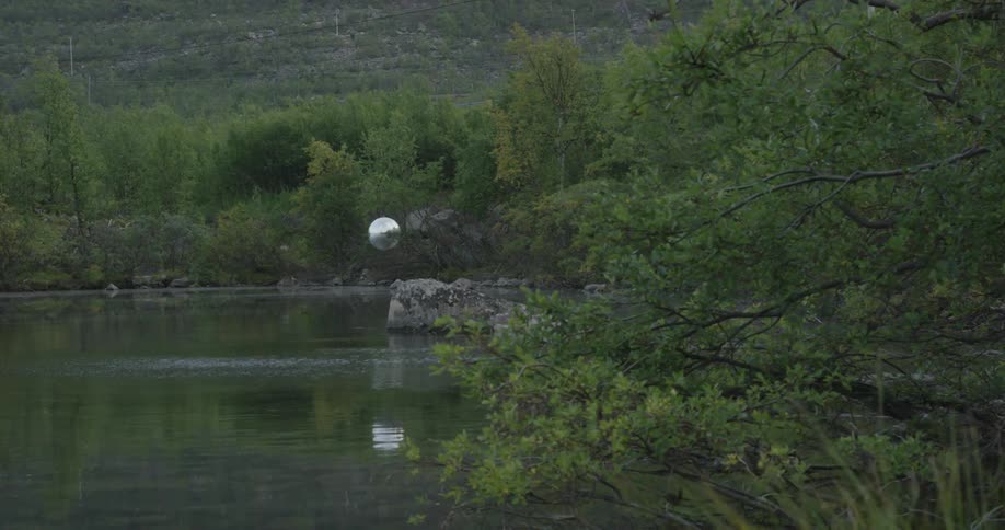 A silver ball floats over a rock in a river