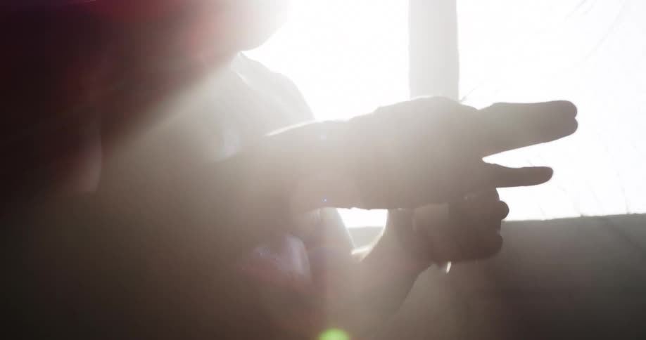 A shirtless man wraps his hand with a white hand wrap while standing in a dimly lit room