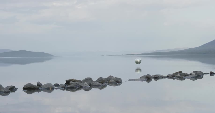 A silver ball hovers over a large body of water and drops in