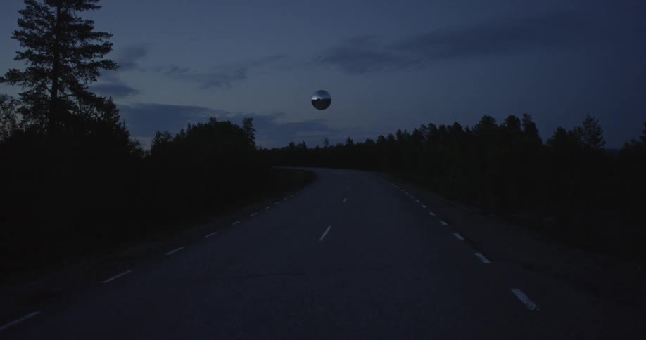 Silver sphere hovering across an empty road