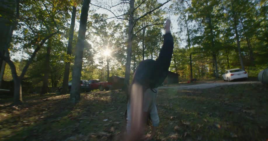 A girl does cartwheels in a forest area while her friend stands and watches