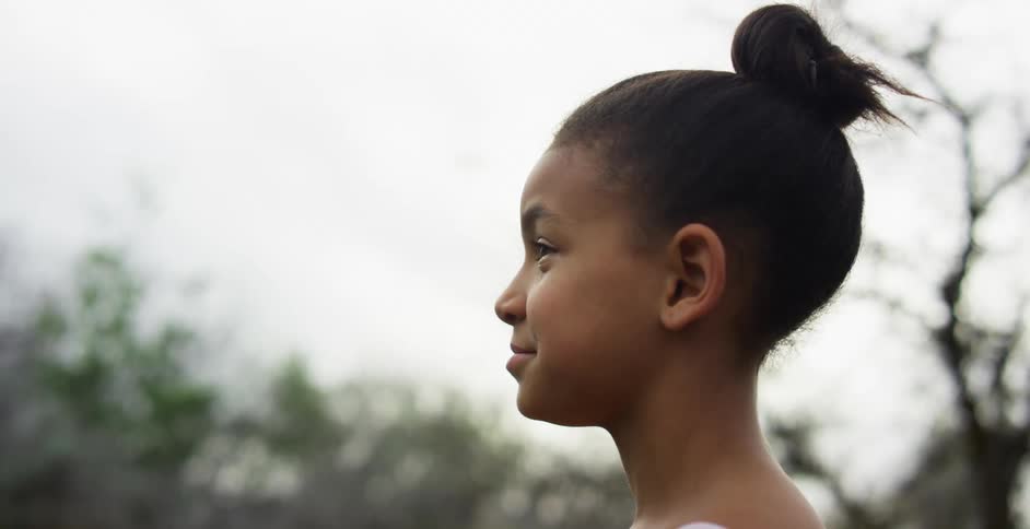 A young black girl stands outdoors with a pleasant smile on her face
