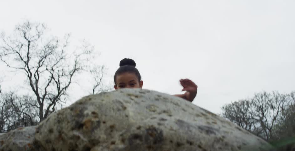 A little girl climbing over a big rock outside
