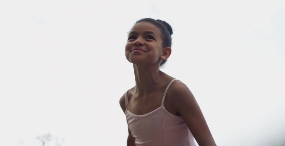 A little girl climbs up a rock and raises her hands in to the air