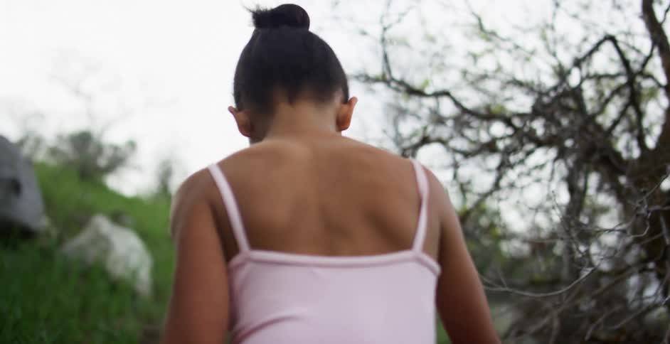 Black girl with a pink ballet dress walks uphill on a cloudy day