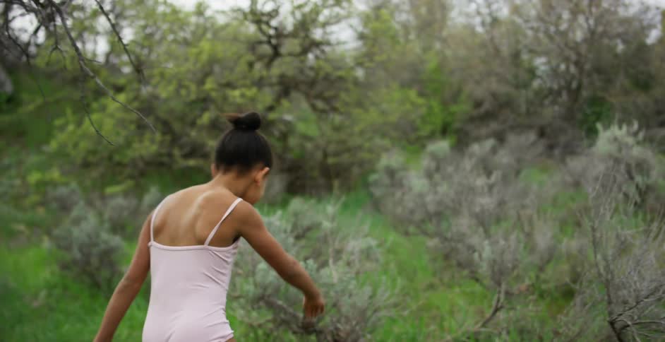 A young girl in a pink leotard runs and dances through a forest