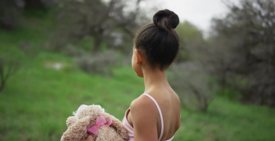 A young girl stands in a forest area holding a stuffed animal