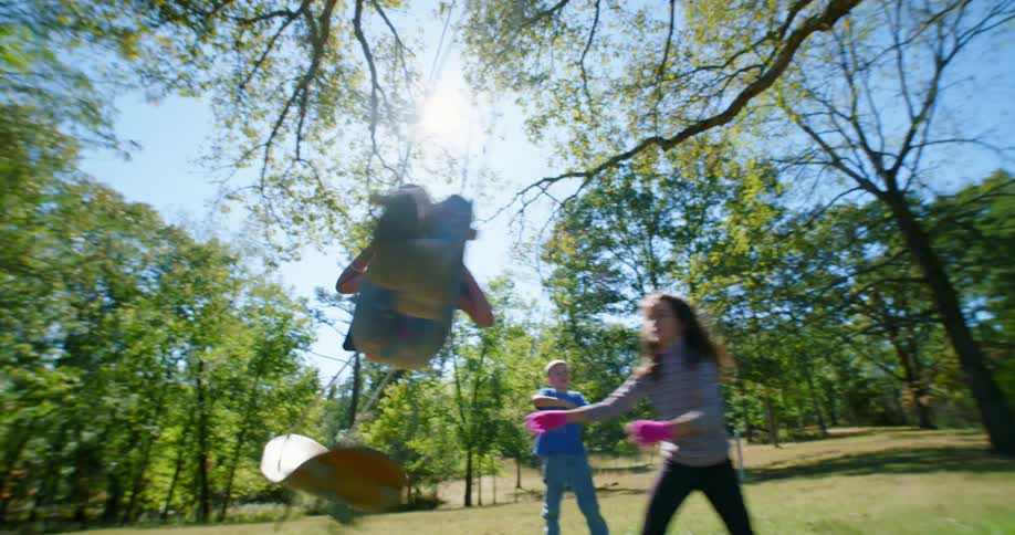 A brother watches as his sister pushes their other sister on a swing