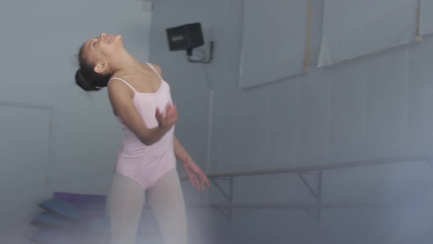 A girl smiles and laughs as she practices ballet in a ballet studio