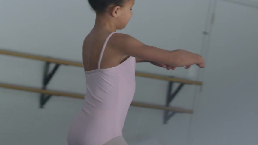 Ballerina wearing pink twirls near wall mounted dance bar