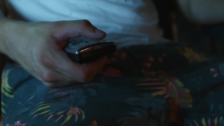 A man sitting and pushing buttons on a remote control