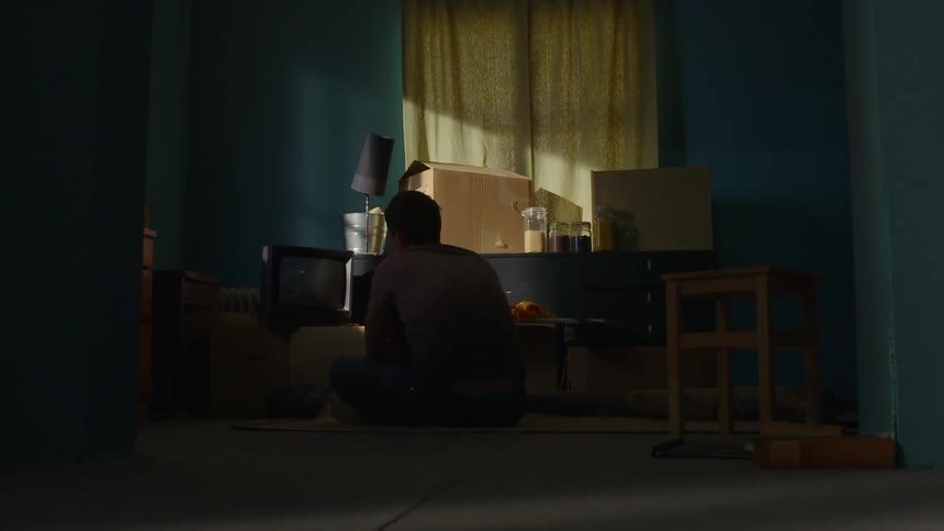 Man sitting on the ground cracks up in a dim lit room