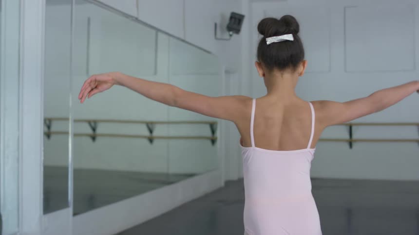 Young female dancer dances and does flip in front of wall mirror in dance studio