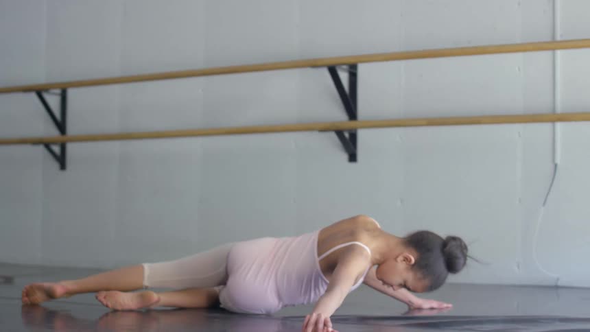 A girl practices ballet movements on the mats of a ballet studio